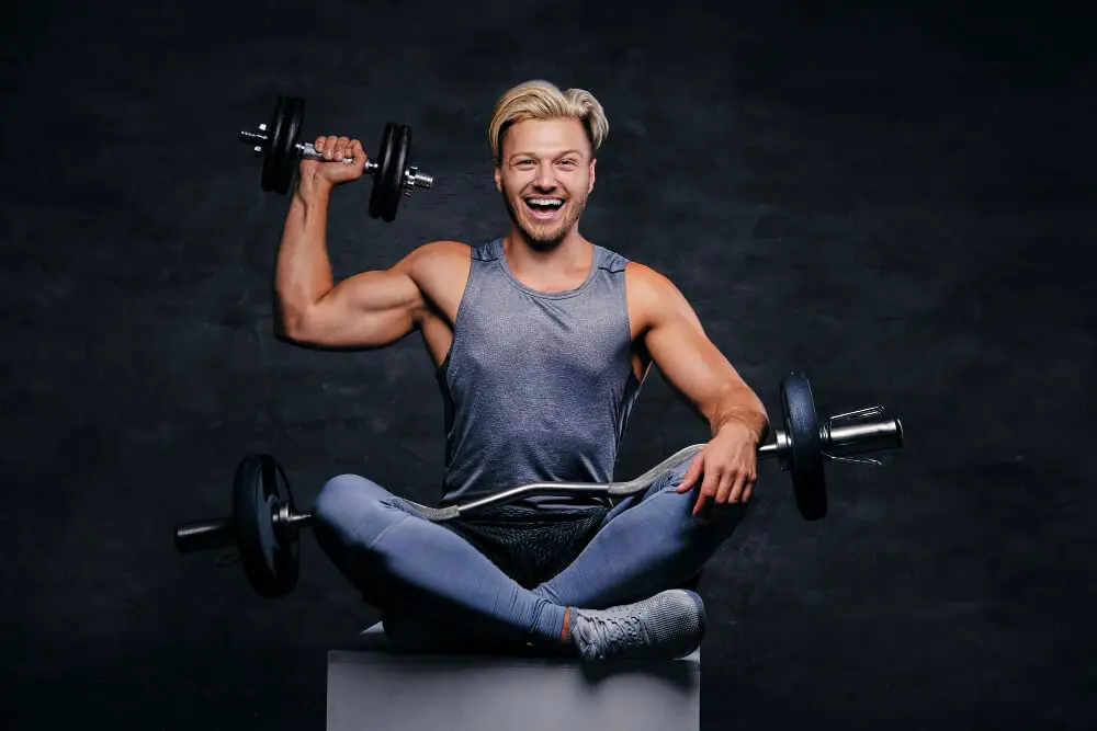 handsome blond sporty male sitting while holding dumbbells