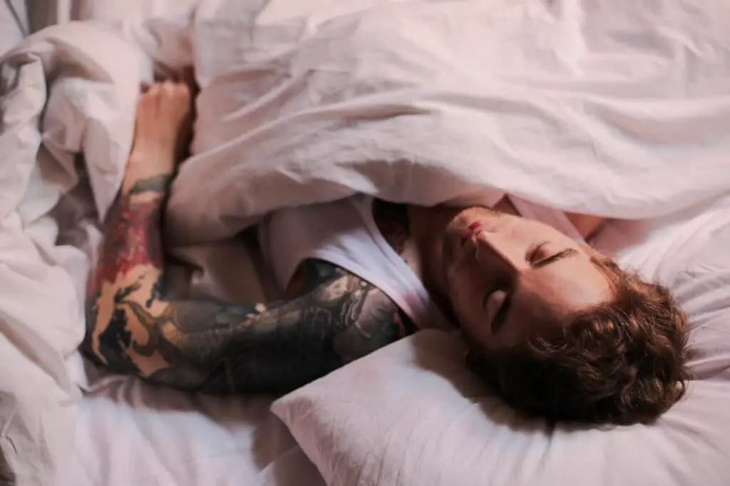 man sleeping in bed with tatoos in his body