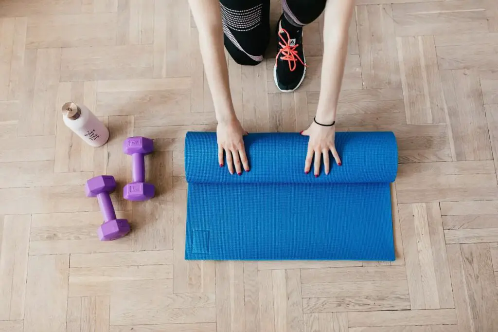 sportswoman unfolding sport mat on wooden floor