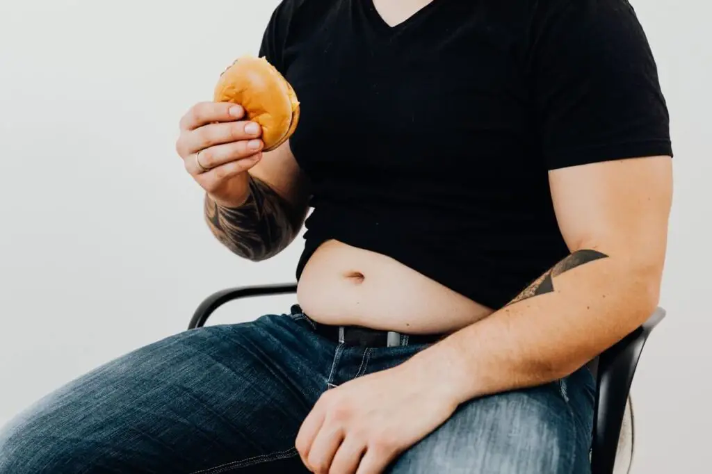a man in black shirt sitting while holding a hamburger