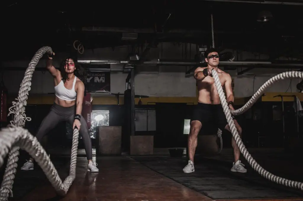 man and woman holding battle ropes in the gym