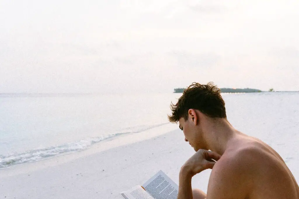 best activities for ectomorphs: shirtless man reading a book while sitting at the beach
