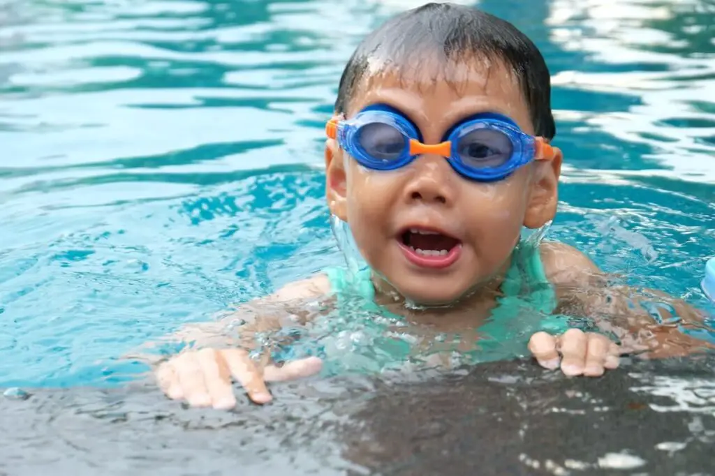 toddler swimming in pool while wearing goggles