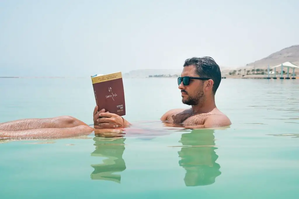 man wearing sunglasses and reading book on body of water
